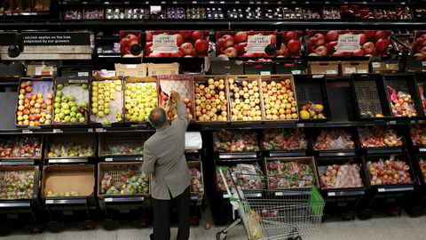 En mann velger epler i en Asda-butikk nordvest i London. Den WalMart-eide kjeden kan nå bli fusjonert med Sainsbury's.