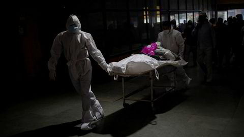 Helsearbeidere frakter liket til en 55 år gammel mann som er død som følge av koronaviruset rett før han skal kremeres. Bildet er tatt i et krematorium i New Delhi den 4. februar i år.