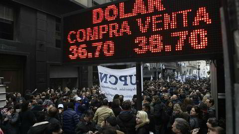 Statsansatte protesterer i Buenos Aires mot planlagte nedskjæringer og nedbemanninger, under et skilt som viser at valutaen peso har mistet halvparten av verdien mot dollar så langt i år.