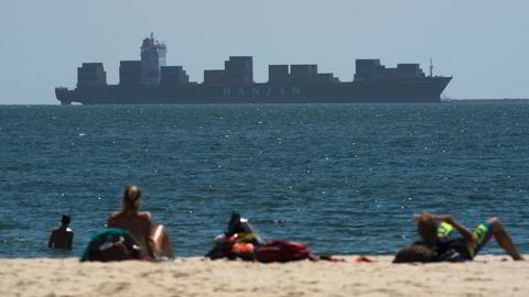 Folk soler seg og slapper av på stranden i Long Beach, California, der flere av det konkursrammede rederiet Hanjins skip ligger utenfor i påvente av at noen kan gjøre opp for lossing av varene. Foto: Robyn Beck/AFP Photo.