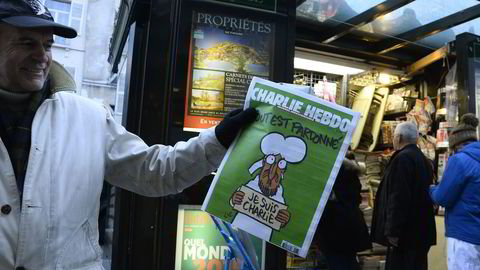 En mann viser frem siste utgave av satirebladet Charlie Hebdo mens andre venter i kø utenfor en aviskiosk i Paris, en uke etter terrorangrepet mot redaksjonen 7. januar. Foto: SCANPIX / AFP PHOTO / BERTRAND GUAY