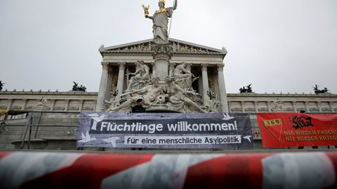 En østerriksk politimann står bak et banner med budskapet «Flyktninger velkomne – for en human asylpolitikk» under en protest foran nasjonalforsamlingen i Wien sist søndag. Foto: Leonhard Foeger / Reuters / NTB scanpix