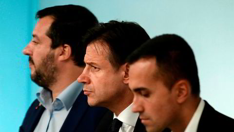 Italias nyvalgte statsminister, Giuseppe Conte, står mellom partilederne for de to regjeringspartiene. Til venstre står Matteo Salvini, leder for Ligaen. Til høyre står Luigi Di Maio, leder for Femstjernersbevegelsen. Vil trekløveret gi etter for presset fra Brussel?