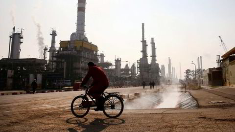 En iransk oljearbeider sykler forbi et oljeraffineri sør for hovedstaden i Iran, Teheran. Foto: Vahid Salemi, AP/NTB Scanpix