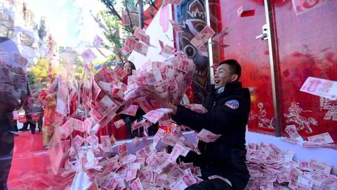 Gjeldsoppbyggingen i Kina og mange andre land i verden bekymrer stadig flere eksperter. På bildet forsøker en mann å fange 100-yuan-sedler i et glassbur i en park i Hangzhou i forkant av årets vårfest. Foto: China Out/Reuters/NTB Scanpix