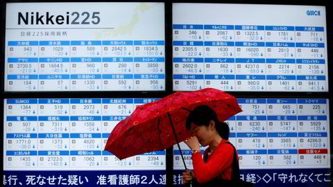 En dame med paraply passerer et meglerhus i Tokyo med en skjerm som viser aksjekurser. Arkivfoto: Toru Hanai/Reuters/NTB scanpix