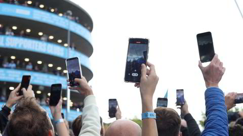 Hva gjør det med oss at vi ser verden gjennom mobilen, og følger spillereglene den dikterer? Bildet viser fans som strekker seg for å ta bilde av spillerne på vei inn før forrige Manchester-derby på Etihad.