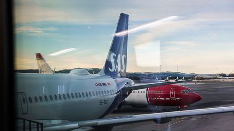 Et parkert SAS-fly passeres av et Norwegian-fly på Oslo lufthavn.