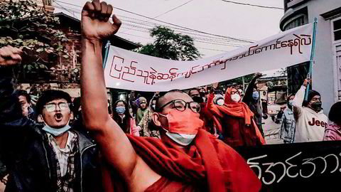 En buddhistisk munk hever den knyttede neven mens han marsjerte under et protestmøte mot militæret etter kuppet i Myanmar i fjor. Telenor-kunder i Myanmar som er regimekritikere frykter konsekvenser ved et salg av mobilvirksomheten.