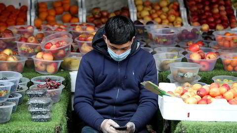 Myndigheter over hele verden deltar i det teknologiske kappløpet om å få kontroll over koronaviruset gjennom innsamling og analyse av befolkningens personlige data. Bildet viser en mann med munnbind ser på mobiltelefonen mens han venter på kunder i Birmingham 30. mars i år.