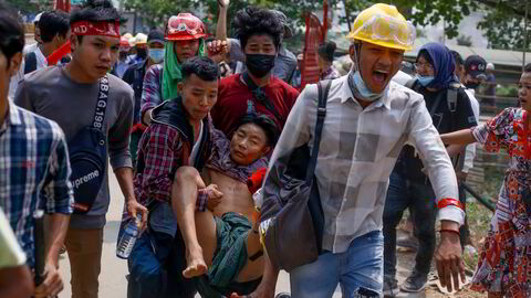Demonstranter bærer en skadet mann etter sammenstøt med sikkerhetsvaktene i Yangon, Myanmar søndag 14. mars 2021.