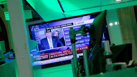 Donald Trumps pressekonferanse overværes på en skjerm på New York Stock Exchange, som holder til på Wall Street. Presidentens løfter om krisetiltak bidro til at indeksene steg tirsdag.