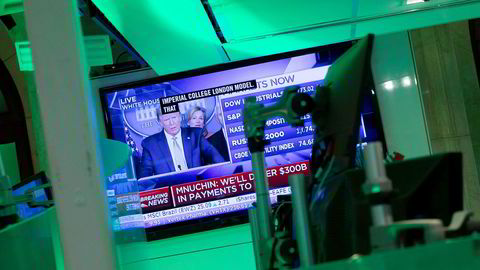 Donald Trumps pressekonferanse overværes på en skjerm på New York Stock Exchange, som holder til på Wall Street. Presidentens løfter om krisetiltak bidro til at indeksene steg tirsdag.