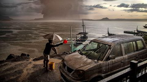 En mann vasker bilen for aske og regnvann etter utbruddet i Taal-vulkanen på Filippinene. Vulkanen ligger på en øy i en innsjø 66 kilometer sør for hovedstaden Manila, og søndag sendte den damp og aske en kilometer opp i luften.