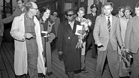 Verdensstjernen Louis Armstrong ankommer Oslo Østbanestasjon i oktober 1955 og blir mottatt med blomsterbukett av jazzmusikeren Gerhard Aspheim (bak til venstre) og Aftenpostens jazzjournalist Stein Kagge (til høyre)