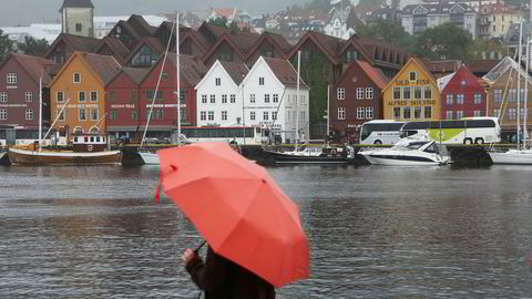 En turist med paraply på en regnværsdag i Bergen med Bryggen i bakgrunnen.